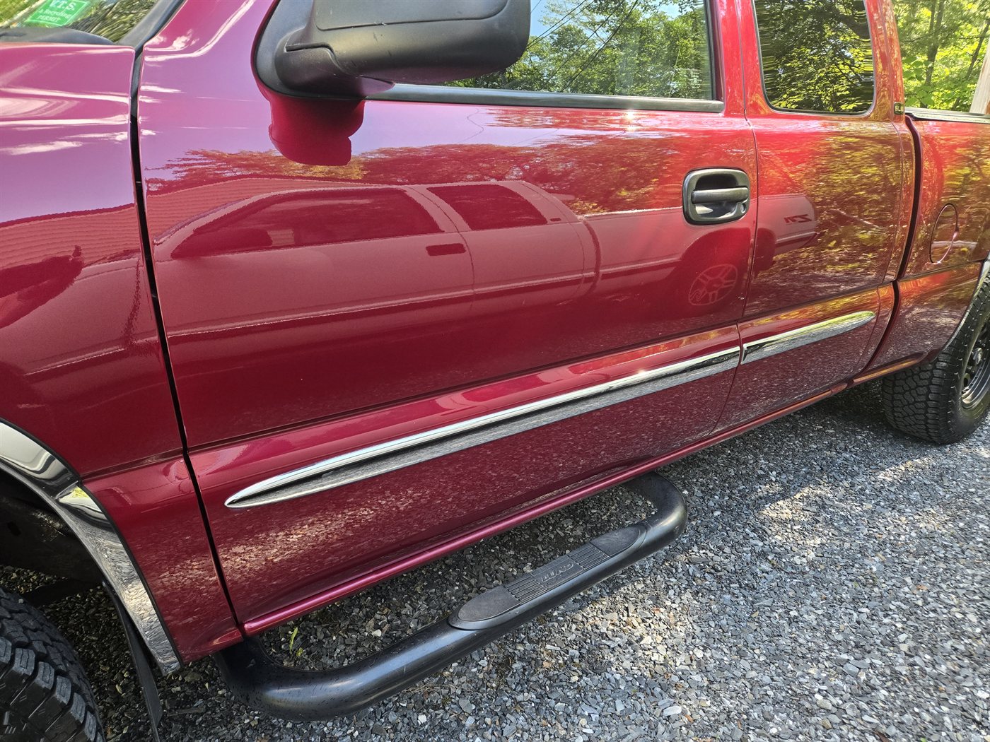 Close-up of Ken's red GMC's shine, with the white Silverado reflected in the paint